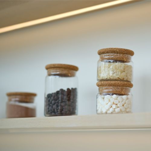 Glazen voorraadpot van 1 liter met vulling en logo, gebruikt in een sfeervolle binnenruimte.